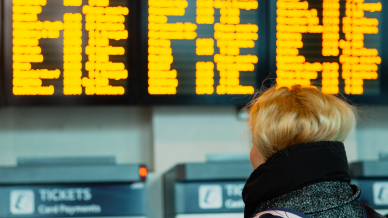 Young woman with blonde hair looking at an information board displaying train times.