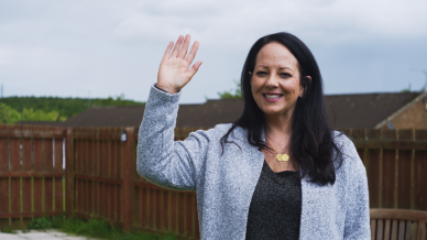 Joanne Hassan waving and smiling at the camera outside