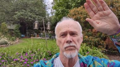 Landscape image of Tony raising his hand with a garden in the background