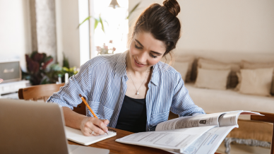 Lady in denim shirt sitting at a table studying with a book, pencil in her right hand