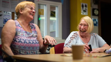 Two ladies sitting at a table with coffee laughing.