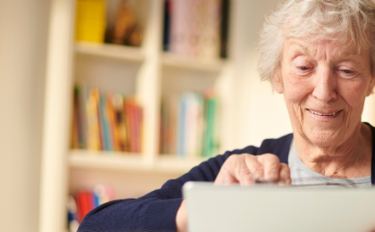 Older lady using a tablet in her living room with a bookcase behind her