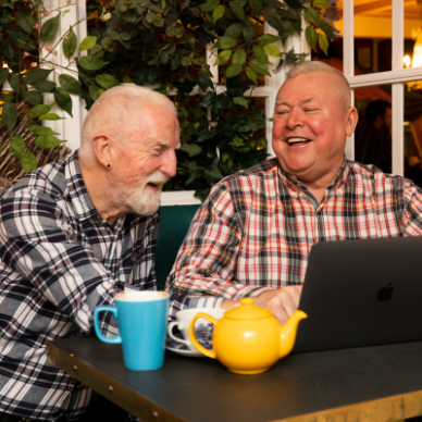Health and Wellbeing - two males sit at a table around a laptop