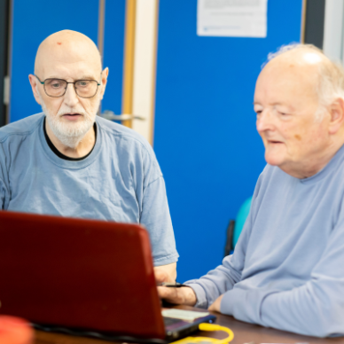 Two men sit around a red laptop