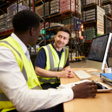 Two colleagues in a warehouse sit next to a computer