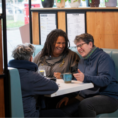 Three learners sitting around a table drinking coffee and laughing