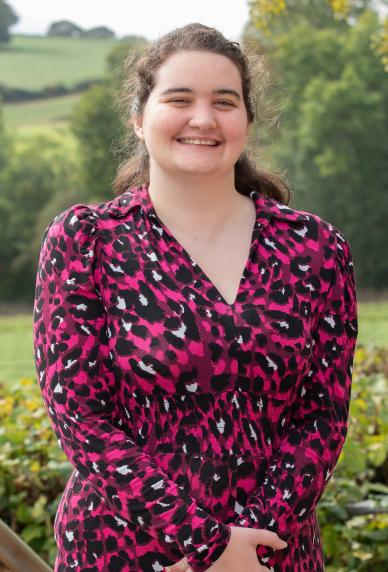 Elen in a pink and black dress standing on the terrace with view of fields in the background