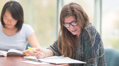 Female learner with a notepad sits at a desk highlighting words in her notebook