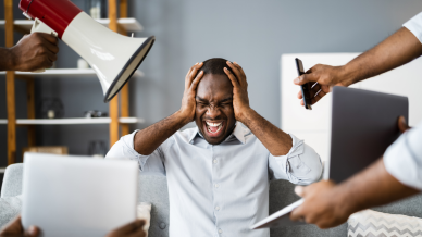 A man holds his head in frustration as he is bombarded with information on a laptop, mobile phone and other media forms