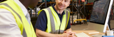 Two colleagues in a warehouse sit next to a computer
