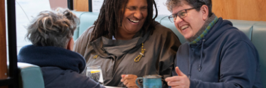 Three learners sitting around a table drinking coffee and laughing